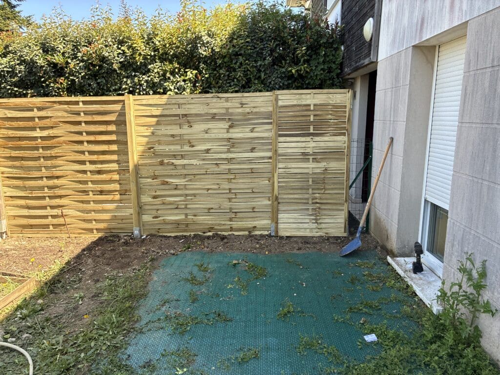 Pose d'une clôture en bois occultante dans un jardin avec dalles de sol et matériel de bricolage.
